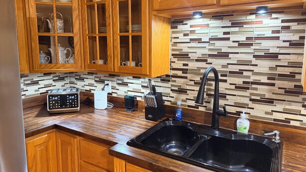 Eine Küche mit Holzausstattung, einem Doppelwaschbecken, einer Spritzschutzwand mit Mosaikfliesenmuster und einer eingebauten Dunstabzugshaube.