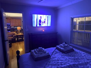 Ein Schlafzimmer mit einem Bett, einem Fernseher, einem Schminktisch und einem Fenster.