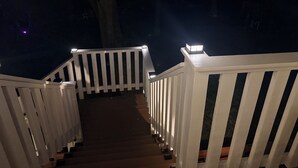 Eine Holztreppe mit weißen Geländern und Beleuchtung am oberen Ende, die zu einem Gebäude führt.