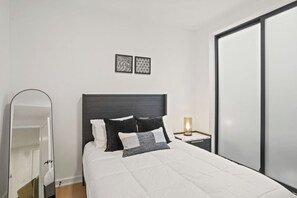 A modern bedroom with a bed, a nightstand with a lamp, a mirror, and two wall art pieces. - Modern DC Stay Steps to Convention Center (Washington)