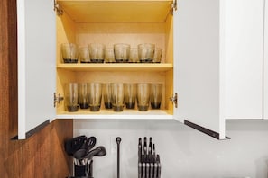 Ein Küchenschrank mit zwei Einlegebögen, auf denen klare Gläser stehen, ein Utensilienhalter mit schwarzen Küchenhelfern sowie ein Metall-Utensilienhalter mit Metallbesteck.