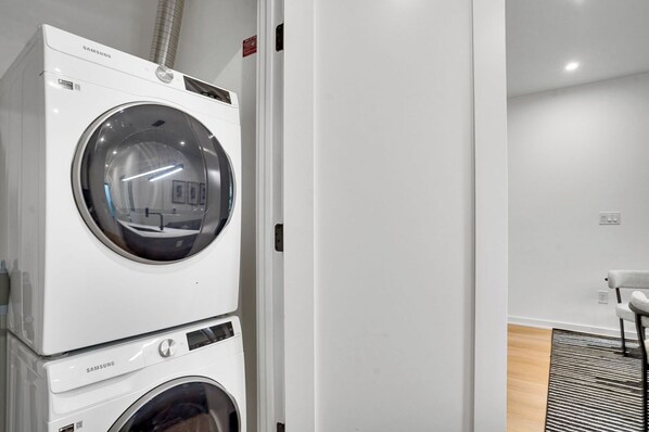 A stacked washer and dryer unit in a modern, minimalistic room with a wooden floor and a chair. - Modern DC Stay Steps to Convention Center (Washington)