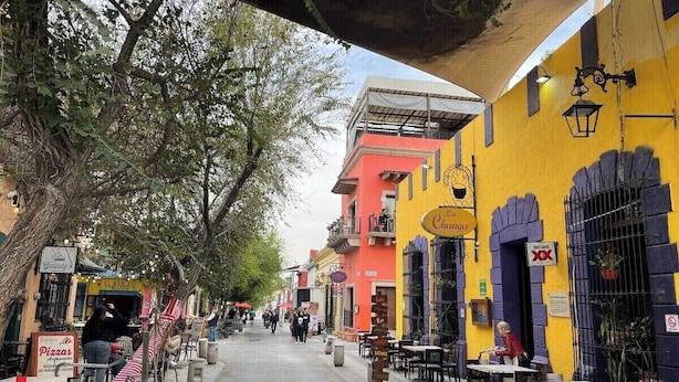 Una calle bordeada de edificios coloridos, con mesas al aire libre y árboles.