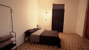 Una habitación pequeña con cama, mesita de noche, luz en la pared y una puerta.