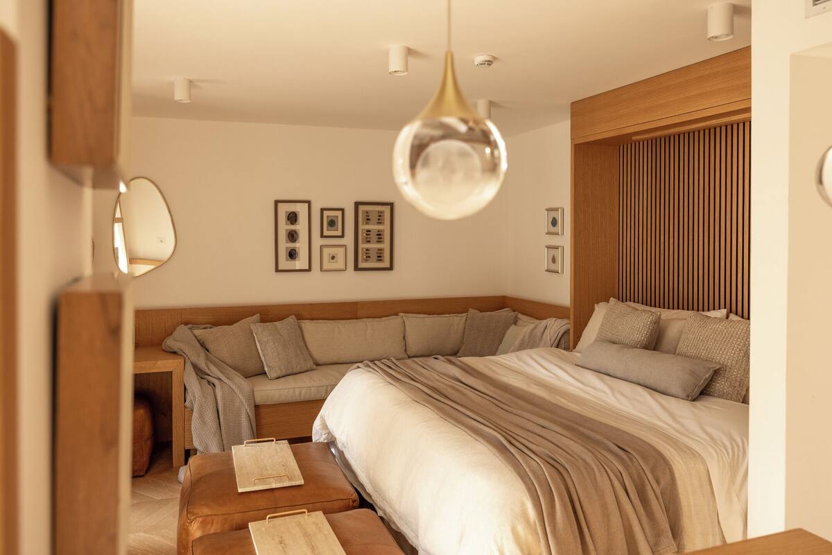 A modern bedroom with a large bed, a bench, a bedside table, and a hanging light fixture.