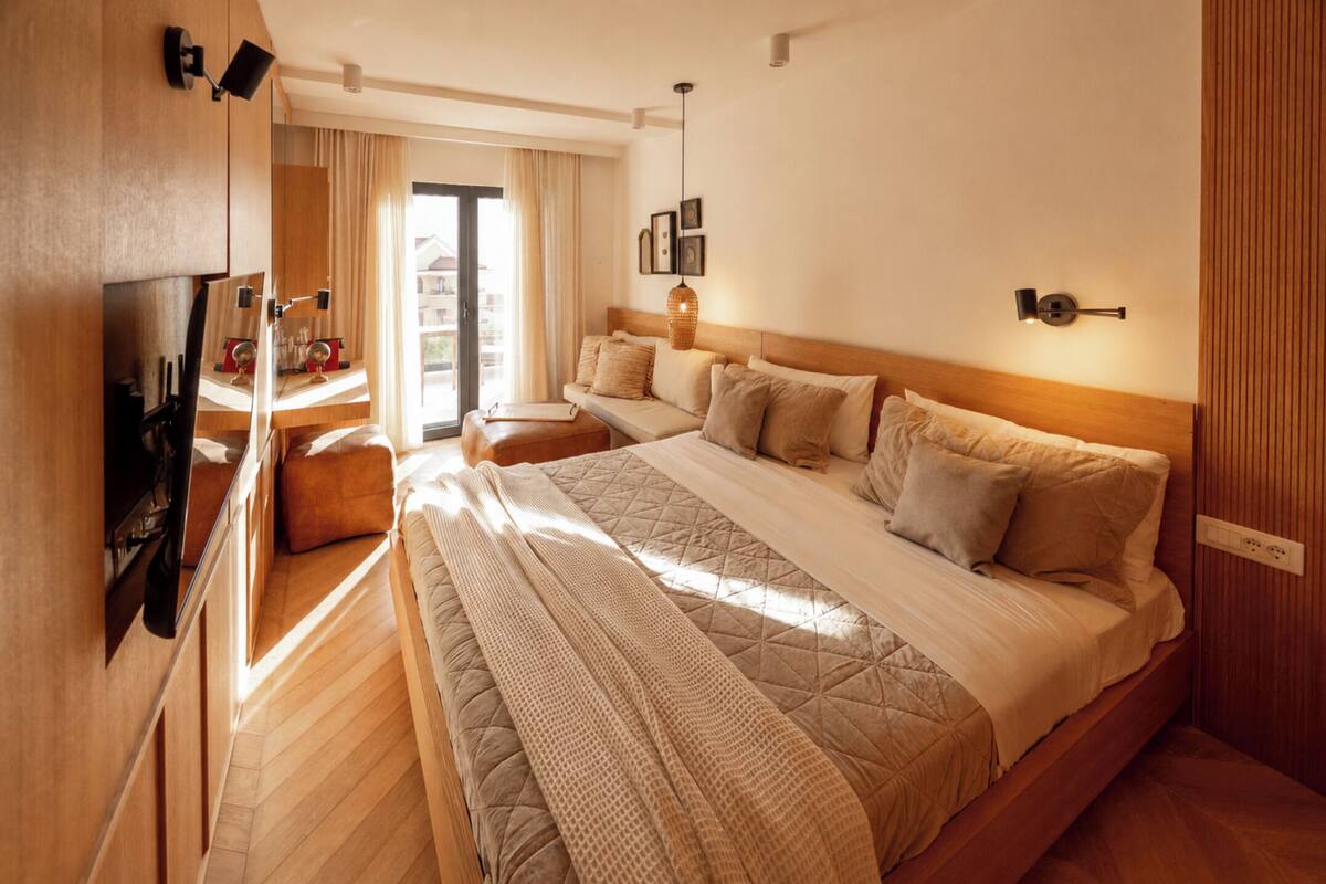 A bedroom with a large bed, a TV, a desk, and a window with curtains.