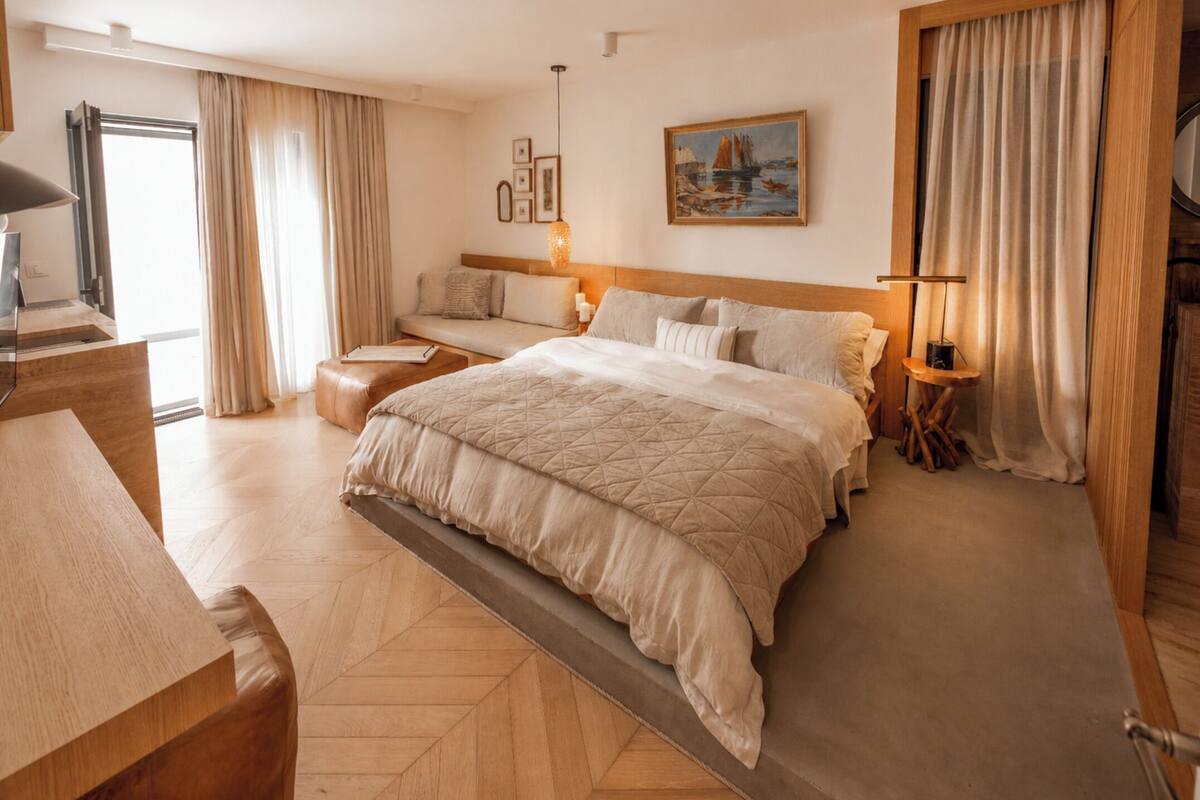 A hotel room with a large bed, a sofa, a desk, and a painting on the wall.