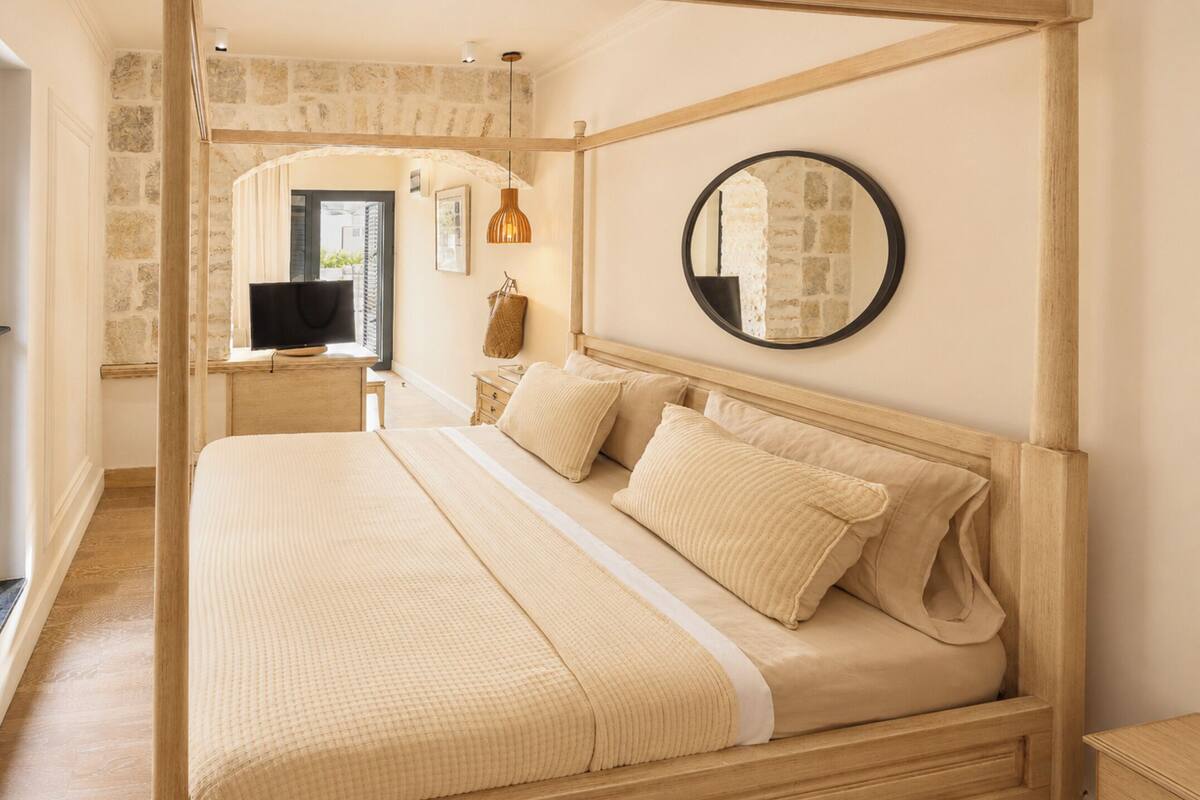 A bedroom with a bed, a round mirror, a television, and a stone wall.