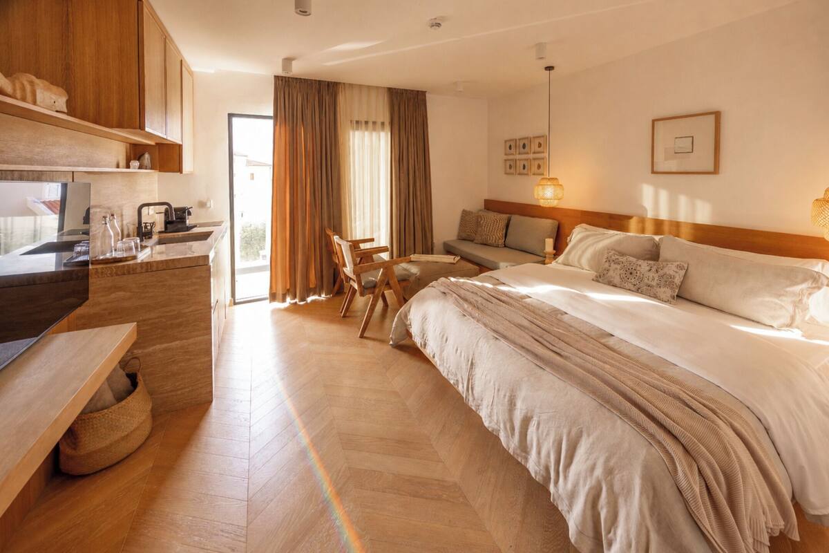 A hotel room with a bed, a sofa, a desk with a computer, and a view of the outdoors.