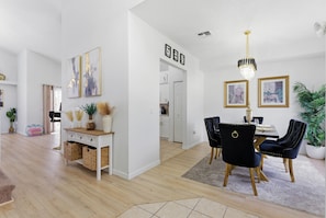 A modern living room with a dining area, white walls, and a chandelier. - 9 Minutes to Disney Pool + Theater + Game Room (Kissimmee)