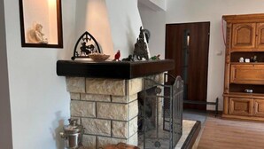 A stone fireplace with a metal grate, a copper pot, and a metal pitcher on a tiled floor. - Comfortable Holiday Villa With a Private Garden (Choczewo)