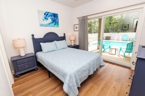A bedroom with a bed, nightstands, a painting, and a view of an outdoor pool area. - Soundside, Ocean views, Private Pool, Comm Amenities-  MS826, Ciao Bella (Corolla)