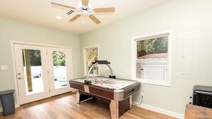 A pool table in a room with wooden flooring, a ceiling fan, and a window with a view of greenery. - Soundside, Ocean views, Private Pool, Comm Amenities-  MS826, Ciao Bella (Corolla)