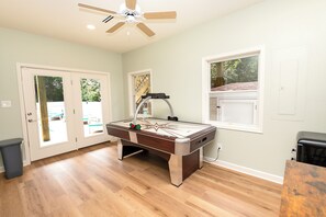A pool table in a room with wooden flooring, a ceiling fan, and a window with a view of greenery. - Soundside, Ocean views, Private Pool, Comm Amenities-  MS826, Ciao Bella (Corolla)