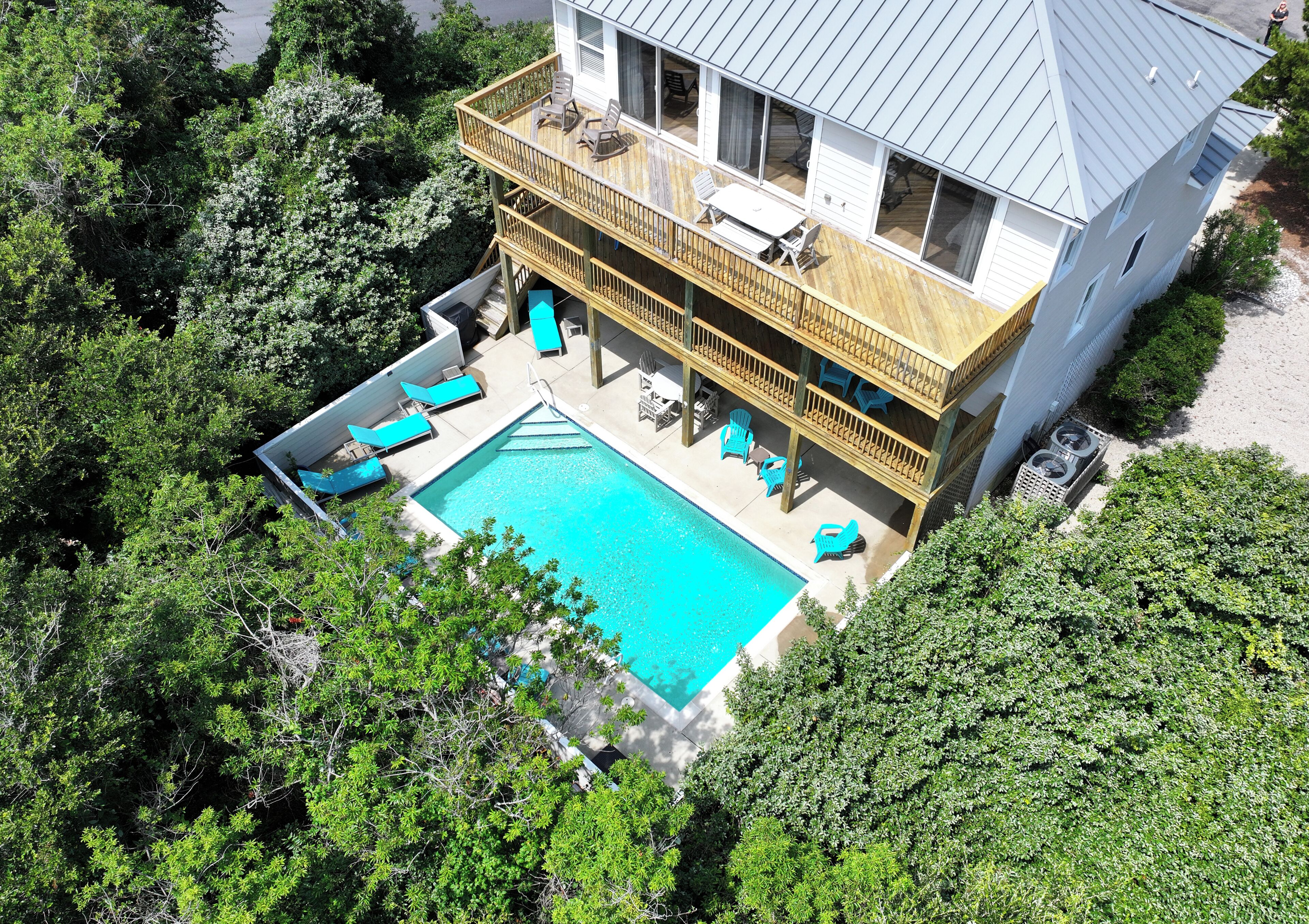 A two-story house with a swimming pool, deck chairs, and a covered patio area.