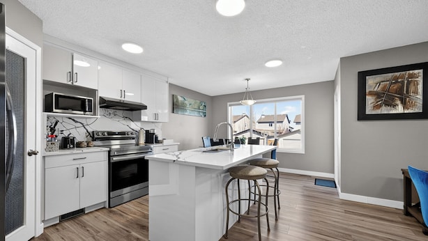 A modern kitchen with white cabinets, a large island, stainless steel appliances, and a view through the window.