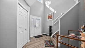 A modern hallway with a wooden floor, white doors, a glass table with a metal frame, and a staircase with a white railing.