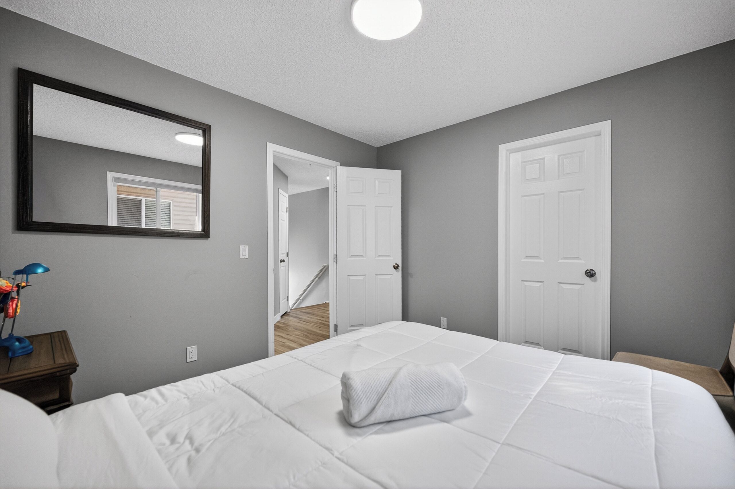 Um quarto com uma cama, uma mesa de cabeceira, um abajur, um espelho e duas portas.