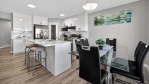 A modern kitchen with white cabinets, a central island, and a dining area with black chairs.
