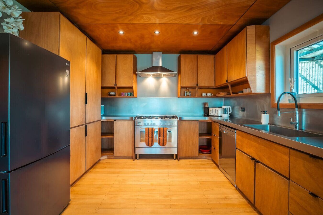 A modern kitchen with wooden cabinets, a stainless steel refrigerator, a gas stove, and a window with a view.