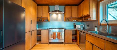 A modern kitchen with wooden cabinets, a stainless steel refrigerator, a gas stove, and a window with a view.