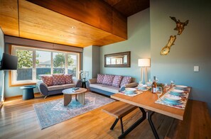 Ein modernes Wohnzimmer mit Sofa, Couchtisch und Esstisch, gedeckt für eine Mahlzeit.
