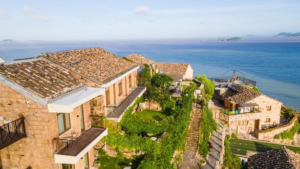 A coastal hotel with stone buildings, a garden, and a view of the sea. - YAOJIA XINGLUOHAIYE RESORT (Taizhou)