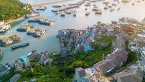 A coastal town with a harbor filled with boats, traditional houses, and a bridge connecting to the mainland. - YAOJIA XINGLUOHAIYE RESORT (Taizhou)