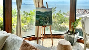 A room with a large window, an easel with a painting, a bed with a white cover, and a potted plant. - YAOJIA XINGLUOHAIYE RESORT (Taizhou)