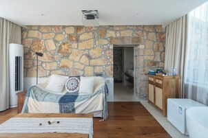 Un dormitorio con pared de piedra, cama con ropa de cama estampada, mesita de noche y vista a otra habitación.