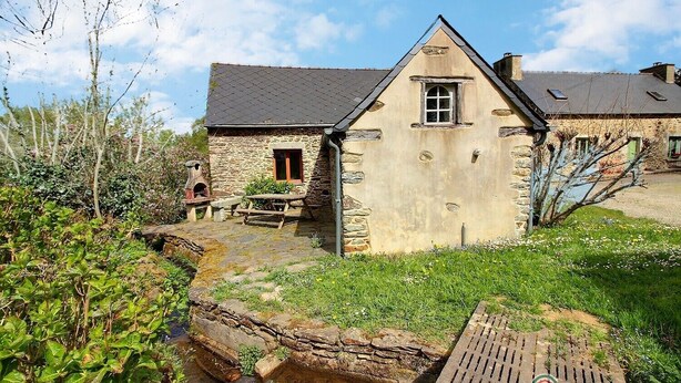 Une maison en pierre avec un toit en pente, un banc en bois et une petite table d’extérieur.