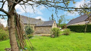 Une maison en pierre avec un toit en pente, entourée d’une pelouse bien entretenue et d’un grand arbre.