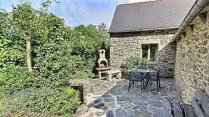 Un bâtiment en pierre doté d’une terrasse carrelée, d’une petite table avec des chaises et d’un four en pierre.