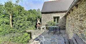 Ein Steinhaus mit einer gefliesten Terrasse, einem kleinen Tisch mit Stühlen und einem Steinkamin.