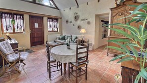 Une pièce avec un plafond haut, une table à manger avec des chaises, un canapé, un buffet en bois et une grande fenêtre avec des rideaux.