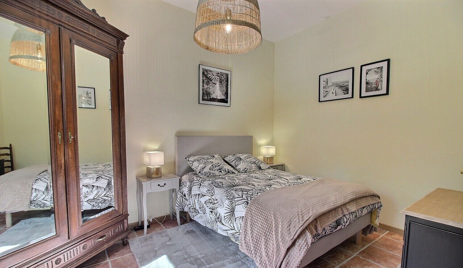 Une chambre à coucher avec un grand miroir, un lit avec une literie à motifs, des lampes de chevet et deux tableaux encadrés accrochés au mur.