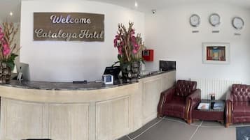A reception area with a reception desk, two red leather chairs, a sign reading 'Welcome Catalina Hotel,' and a window with a view of the street.