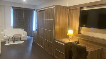 A modern hotel room with a wooden desk, a flat-screen TV, a sofa, and a small round table.