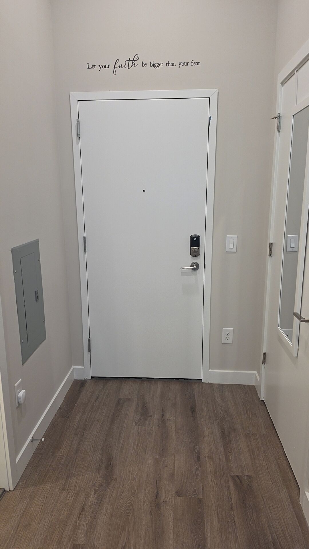 Un couloir avec une porte blanche, un miroir fixé au mur et une citation inspirante.