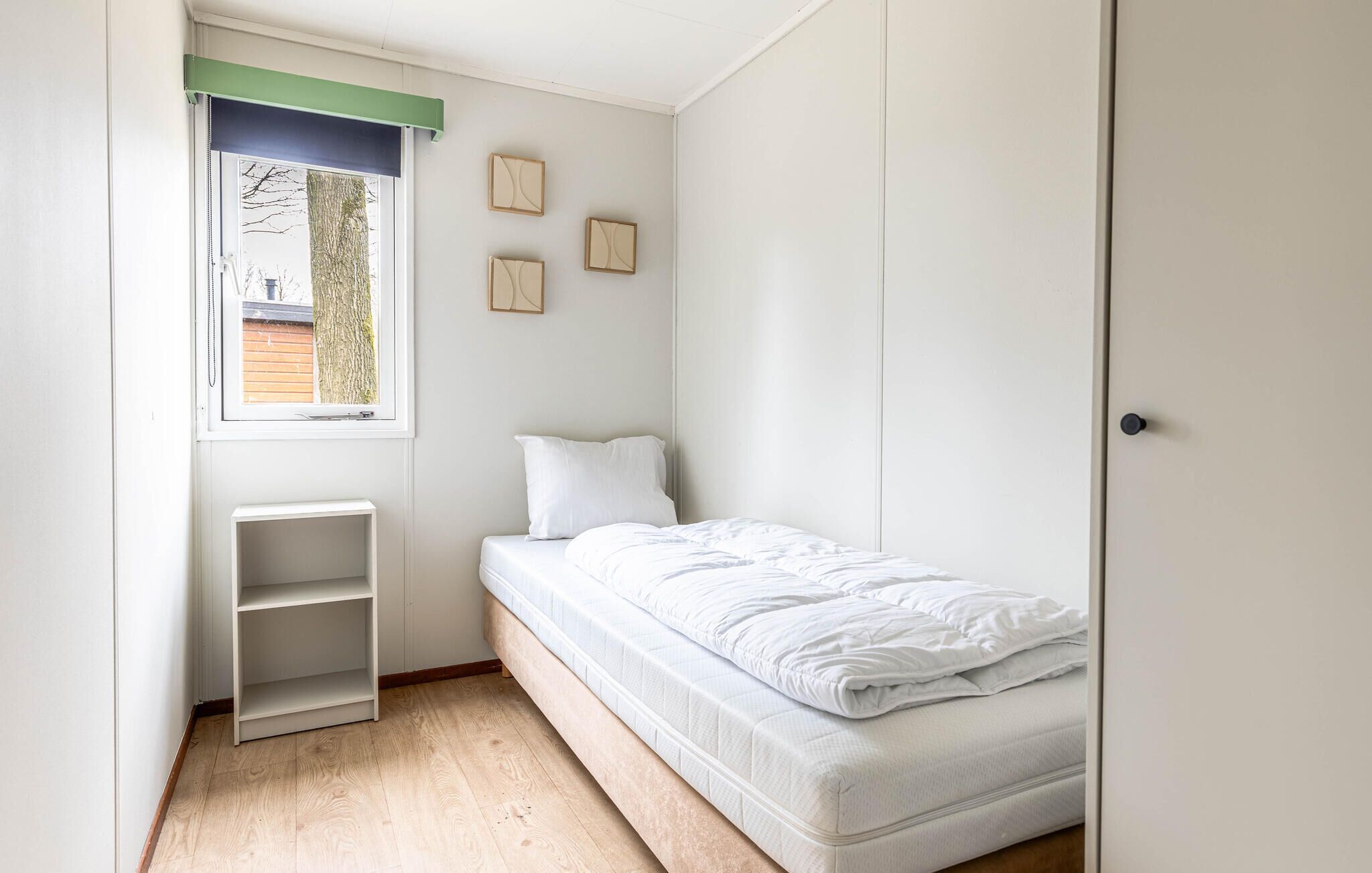 Een kleine kamer met een enkel bed, een raam, een inbouwkast en een kledingkast.