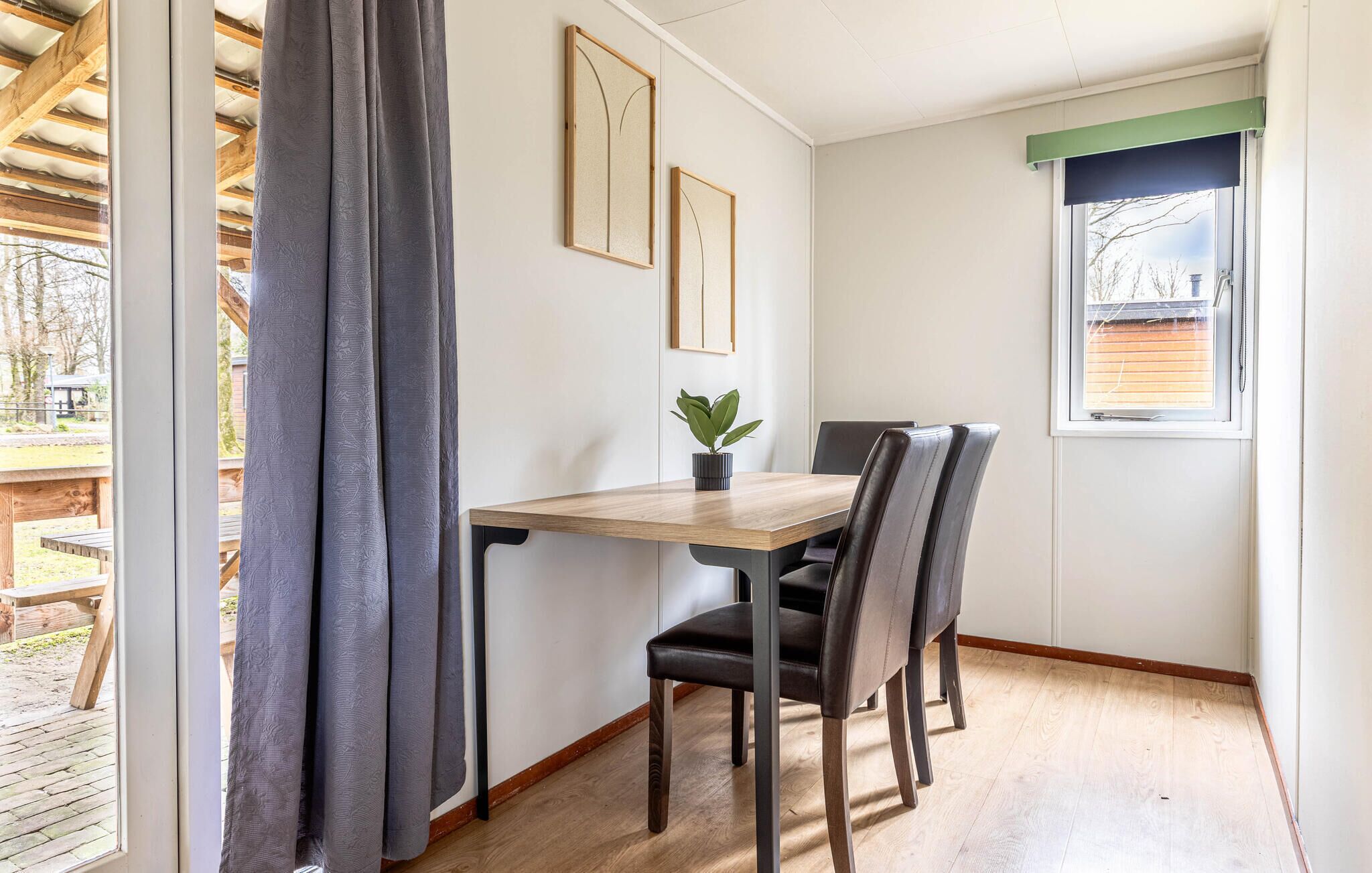 A corner room with a wooden table, two chairs, a potted plant, and framed pictures on the wall.
