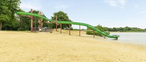 A sandy beach with a green water slide structure.