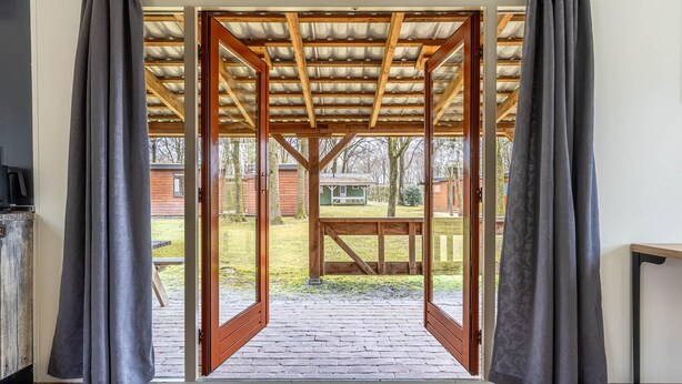 Una struttura in legno aperta con tetto, che conduce a un'area esterna con tavolo e sedie.