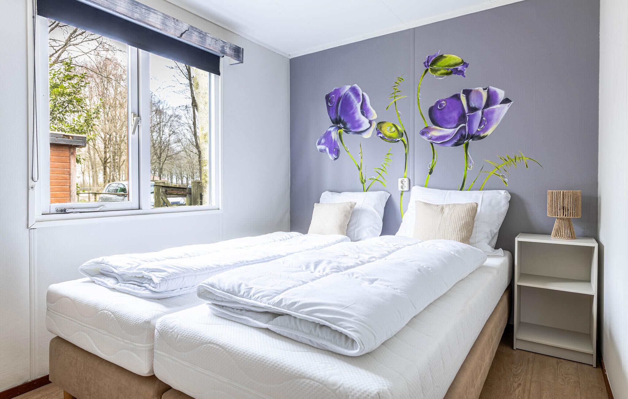 Une chambre avec deux lits, une fenêtre et un mur orné d’une fresque florale.