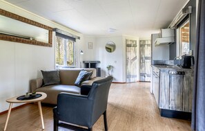 Ein modernes Wohnzimmer mit Sofa, Sessel, einem kleinen Tisch und einer Küchenzeile mit Herd und Spüle.