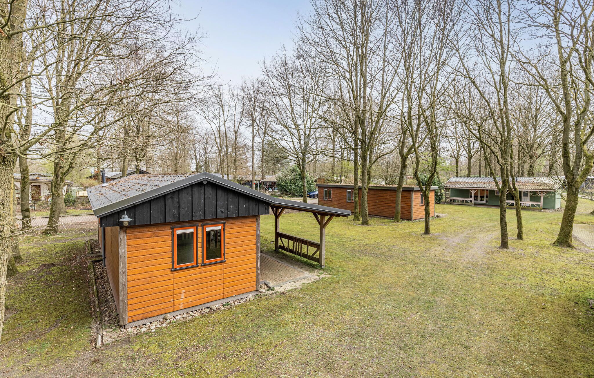 A small wooden cabin with a porch, surrounded by trees and a grassy area.