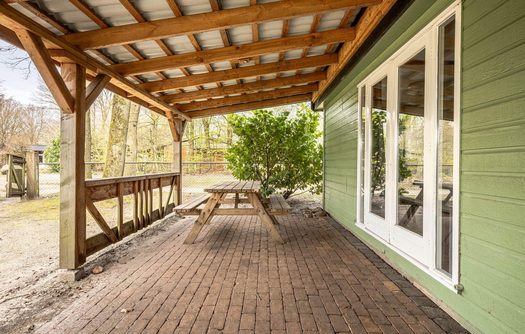 A covered patio with a picnic table, wooden beams, and a green building with large windows.