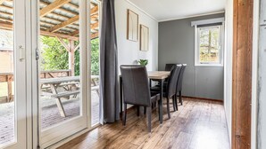 Una habitación con una mesa y sillas de madera, un ventanal con vista a zonas verdes, y una puerta que da a un área exterior con terraza de madera.