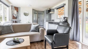 Una sala de estar moderna con un sofá, una mesa de centro y una silla. Hay una zona de cocina con estufa y alacenas.