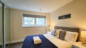 Et hotelværelse med seng, et vindue, et billedværk på væggen og et natbord med lampe.